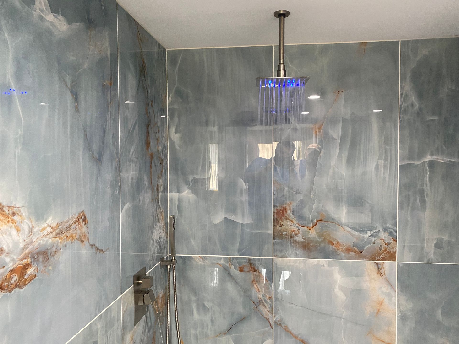 A bathroom with blue tiles and a shower head hanging from the ceiling.