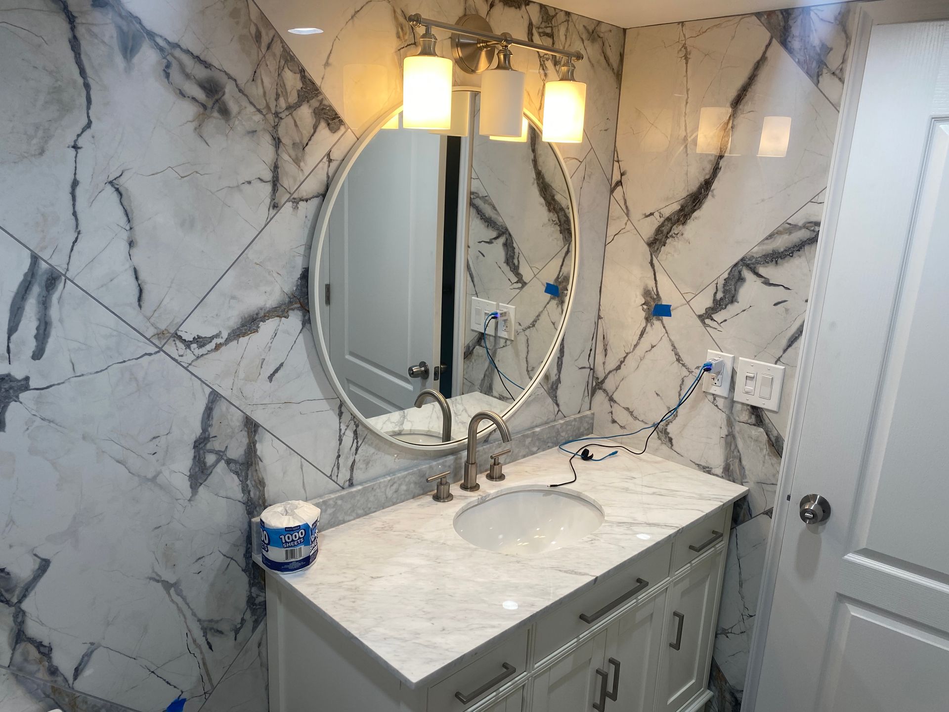 A bathroom with a sink , mirror and marble wall.