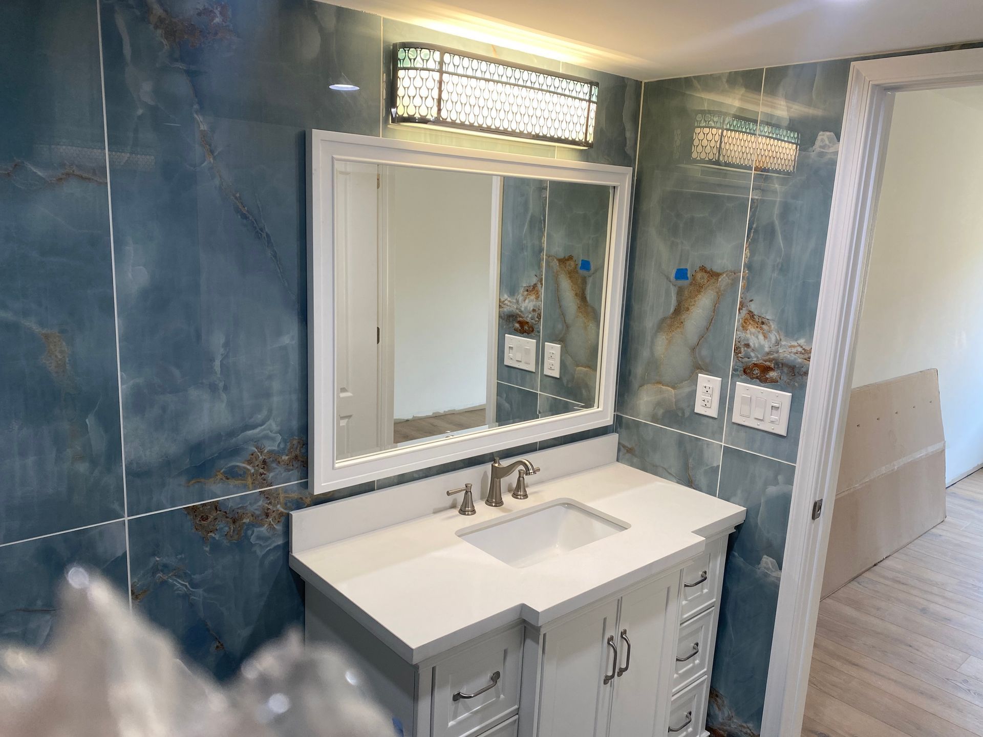A bathroom with a sink , mirror and blue tiles.