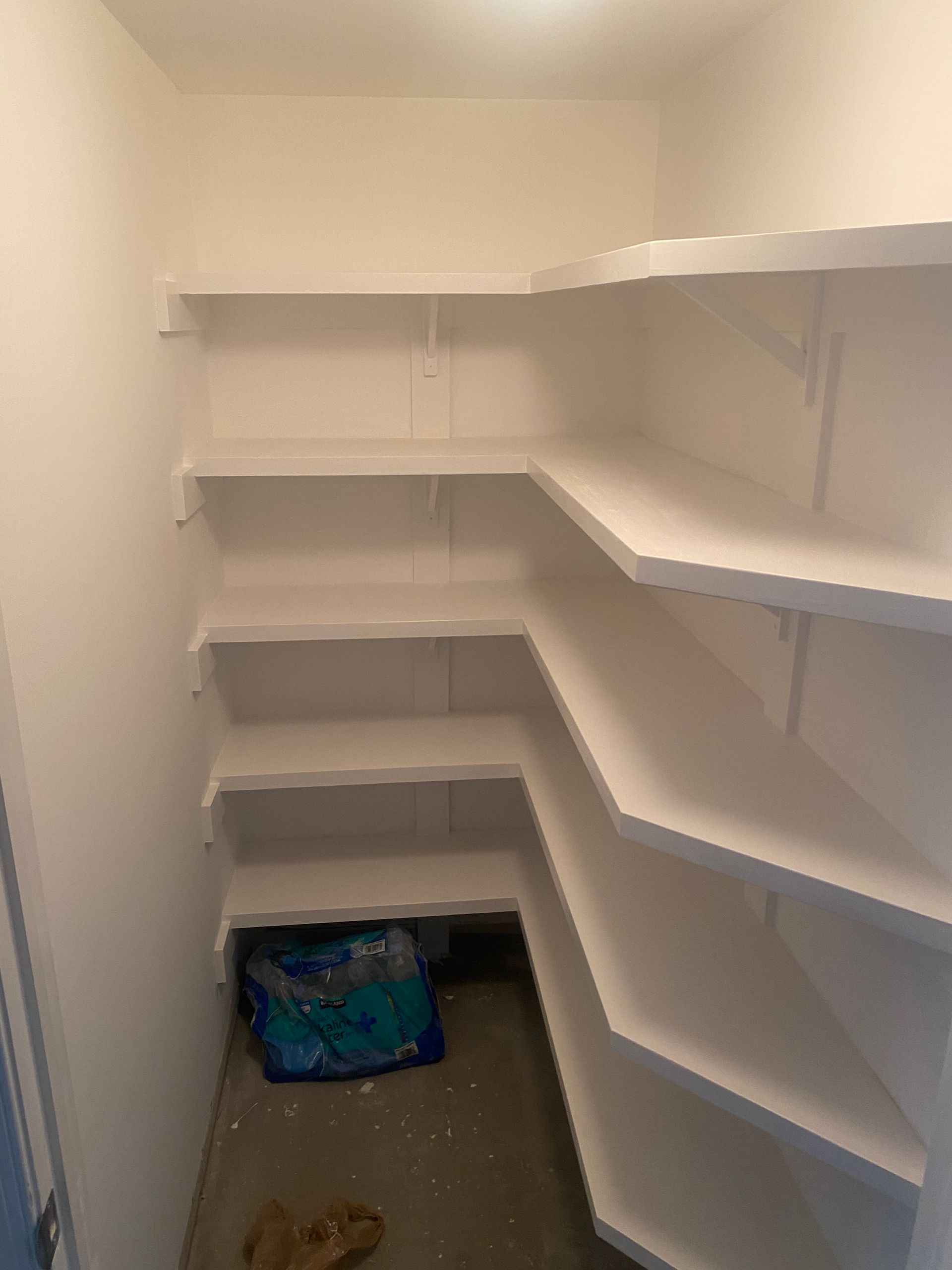 A small closet with white shelves and a blue bag on the floor.