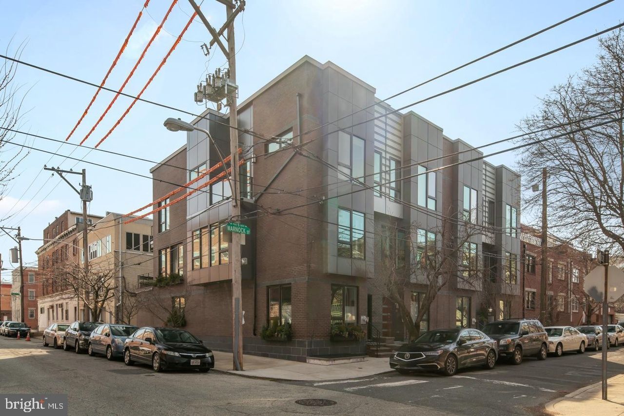 A row of cars are parked in front of a building on the corner of a street.