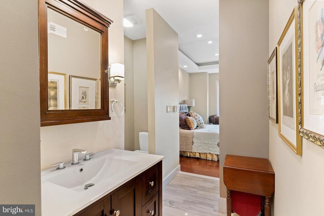 A bathroom with a sink and a mirror leading to a bedroom.