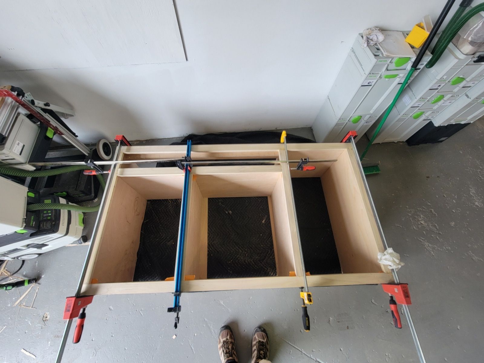 A person is standing next to a piece of wood with clamps on it.