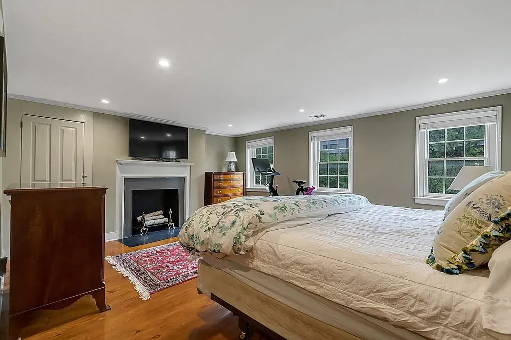 A bedroom with a large bed , fireplace , dresser and television.