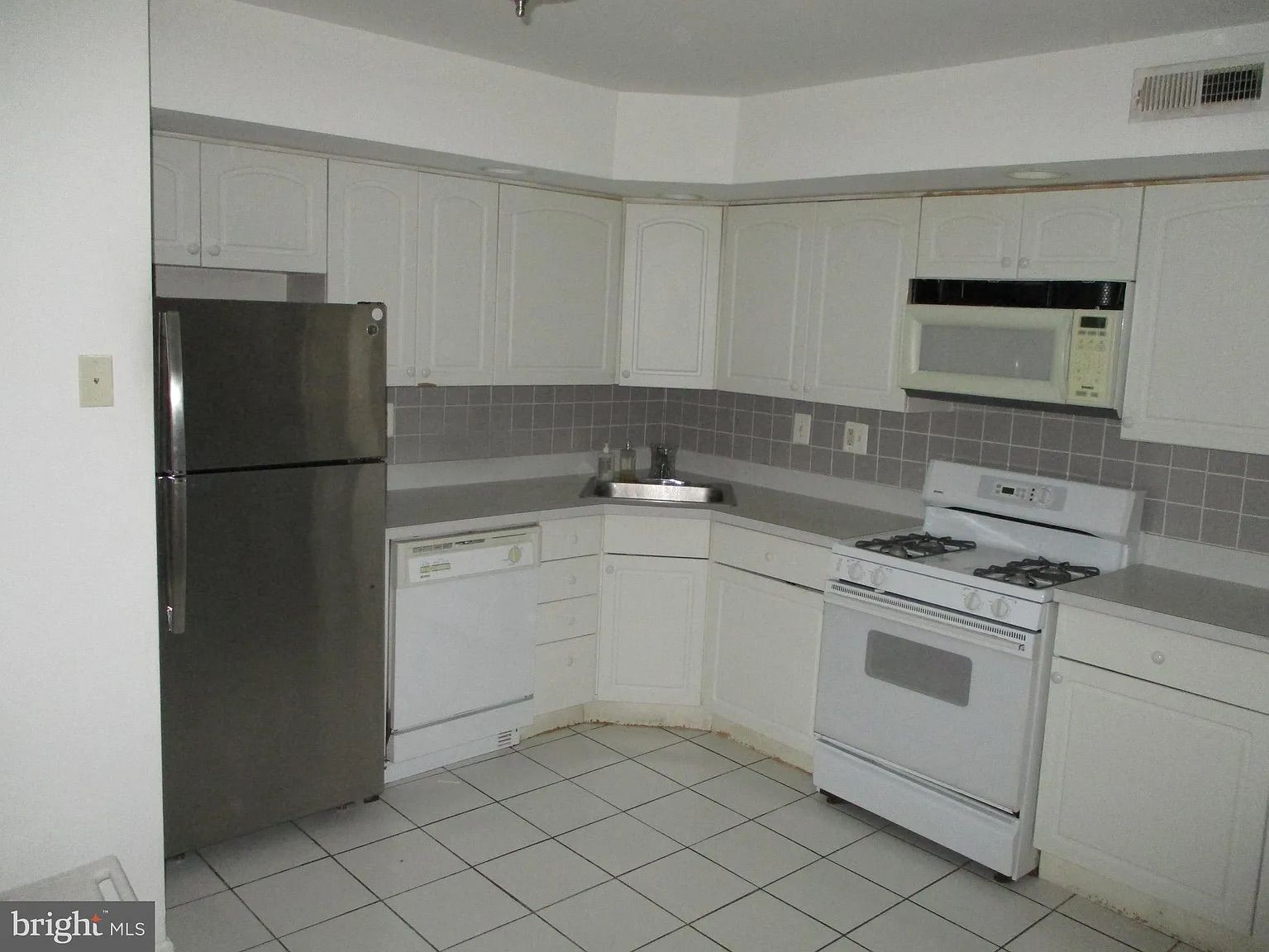 An empty kitchen with white cabinets and stainless steel appliances