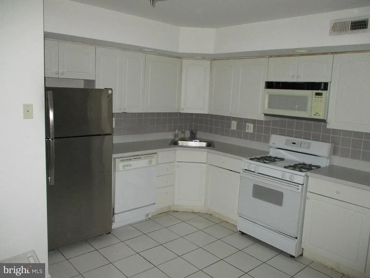 An empty kitchen with white cabinets and stainless steel appliances