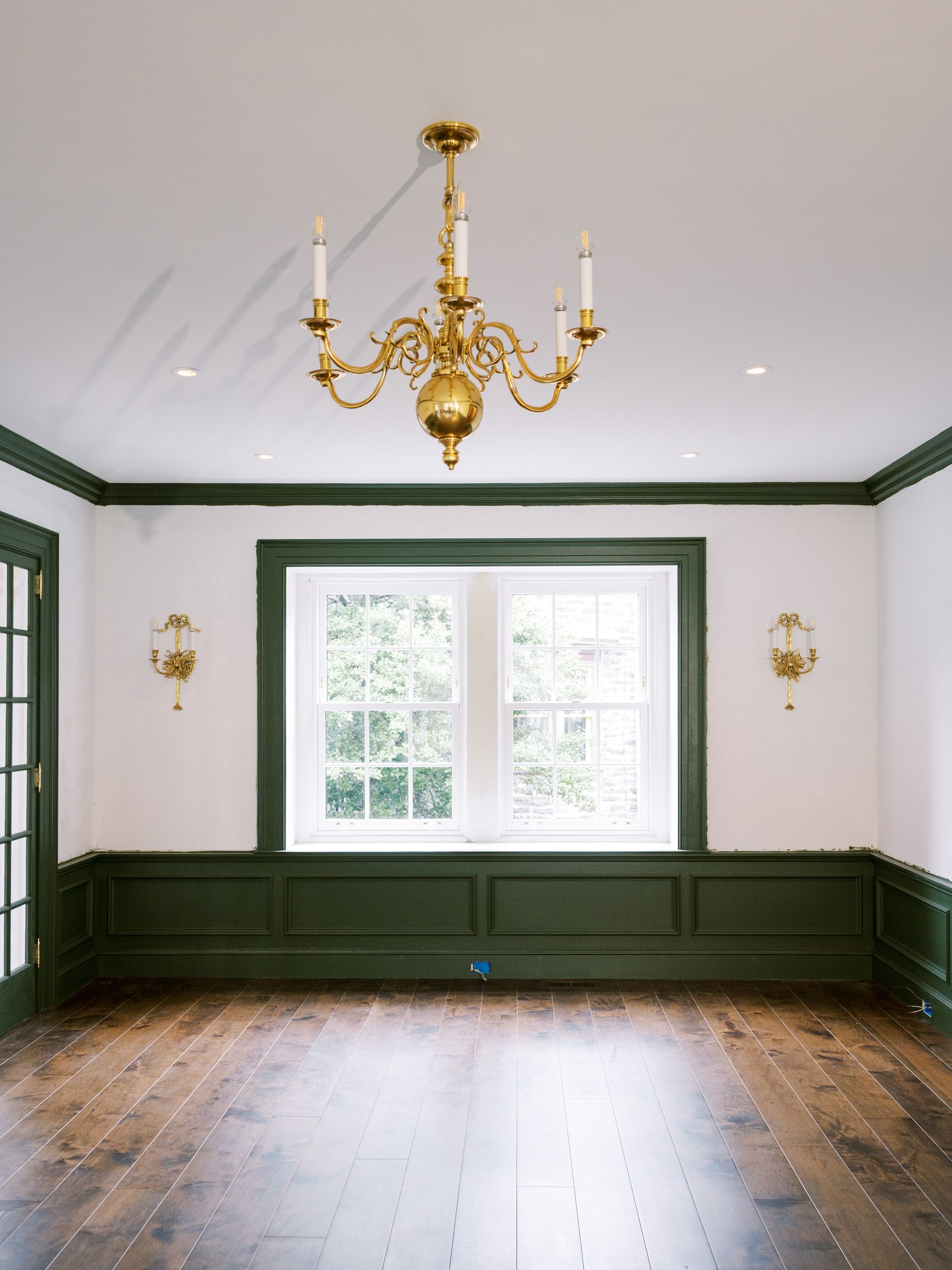 An empty room with a chandelier hanging from the ceiling and a window.