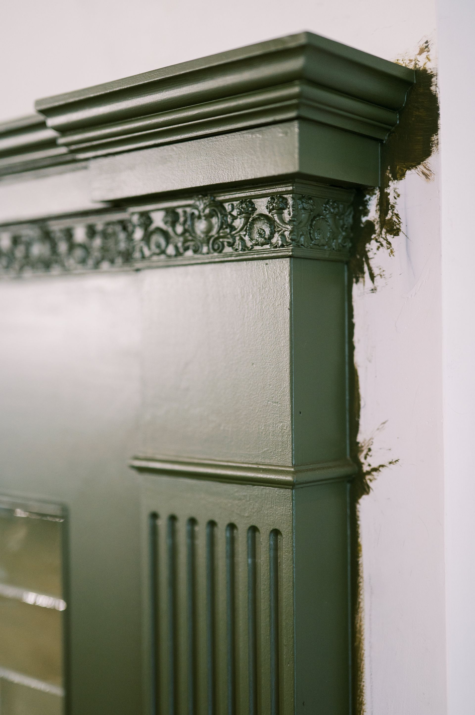 A close up of a green fireplace with a white wall in the background.