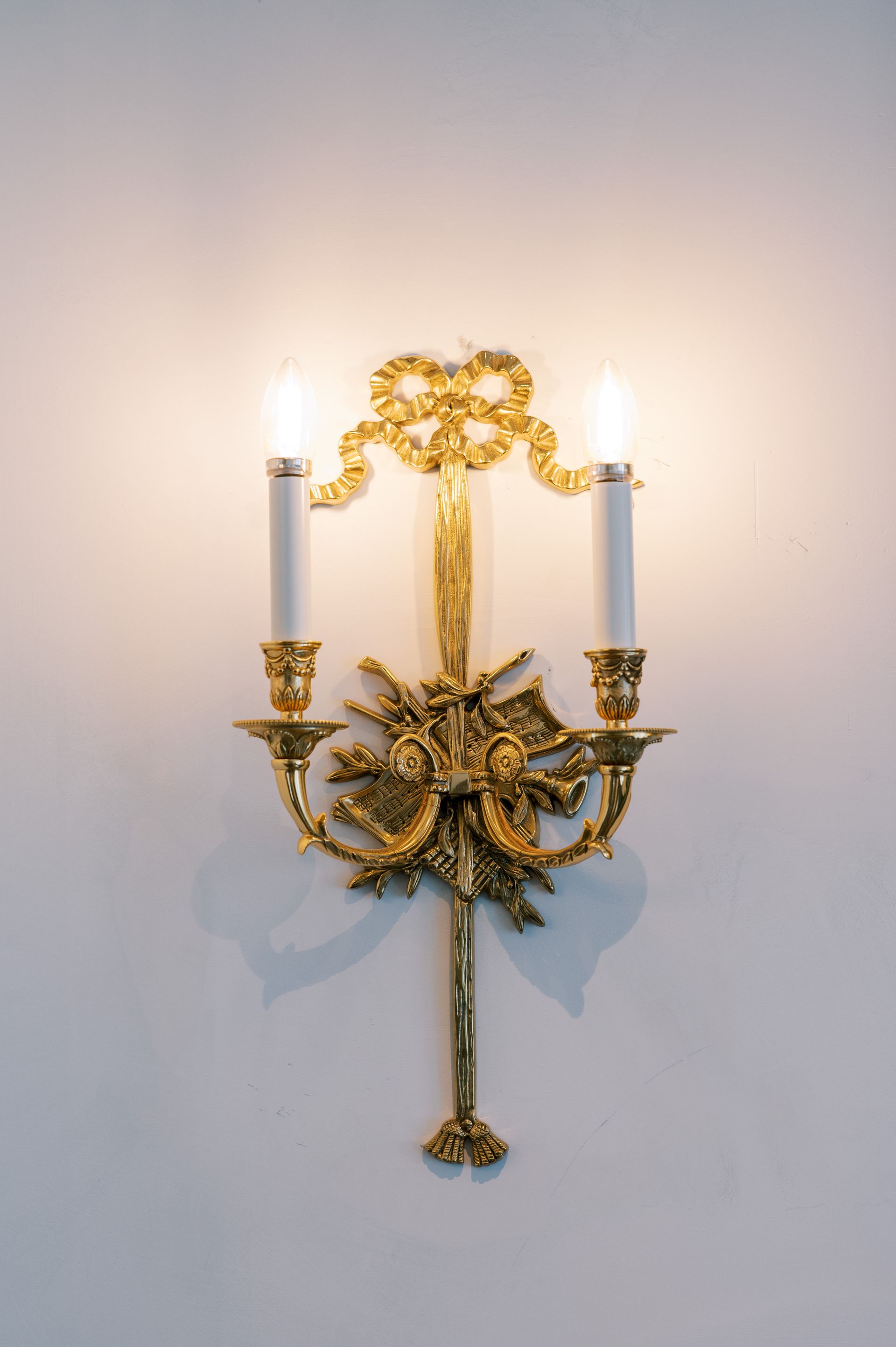 A gold wall light with two candles on a white wall.