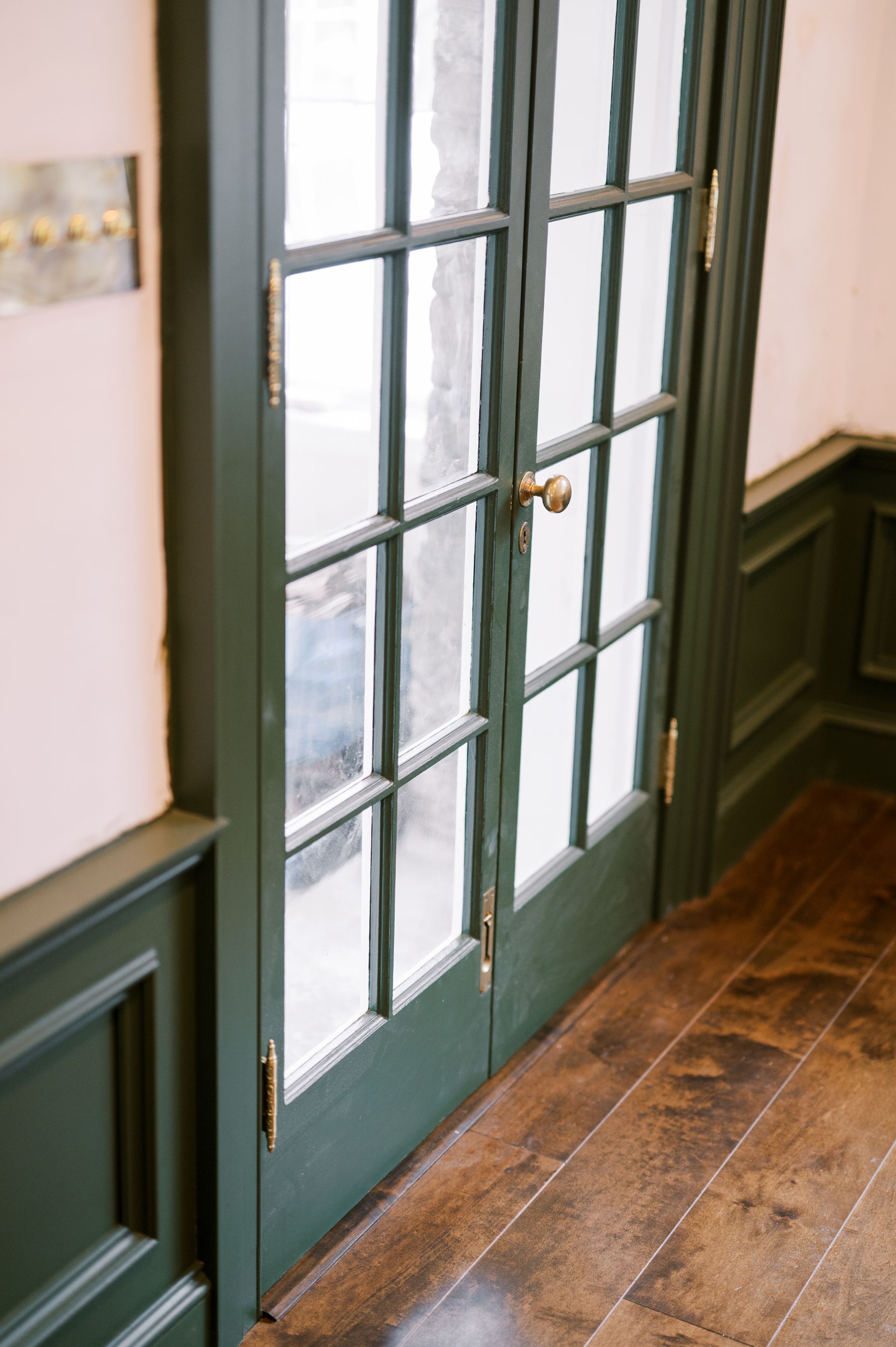 A pair of green french doors in a hallway with wooden floors.