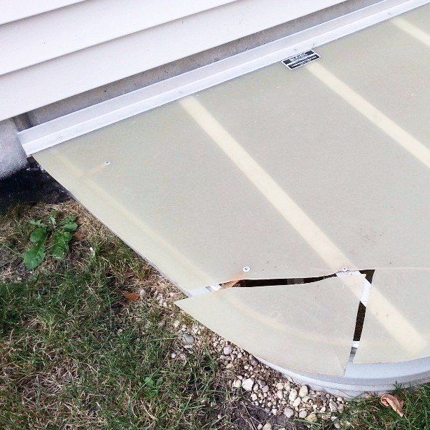 A broken window screen is sitting on the ground next to a house.