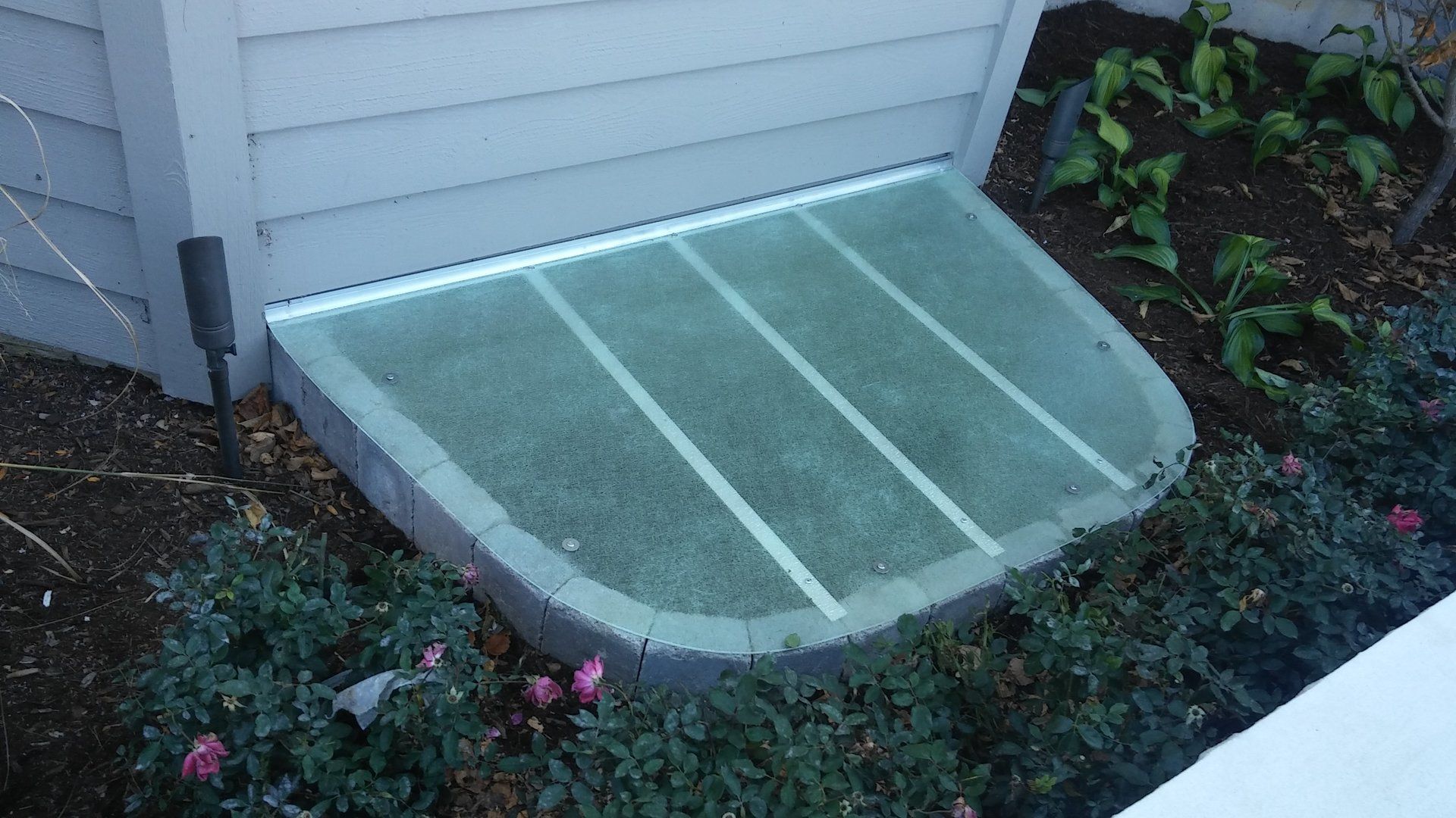 A window well next to a house with a glass cover on it.