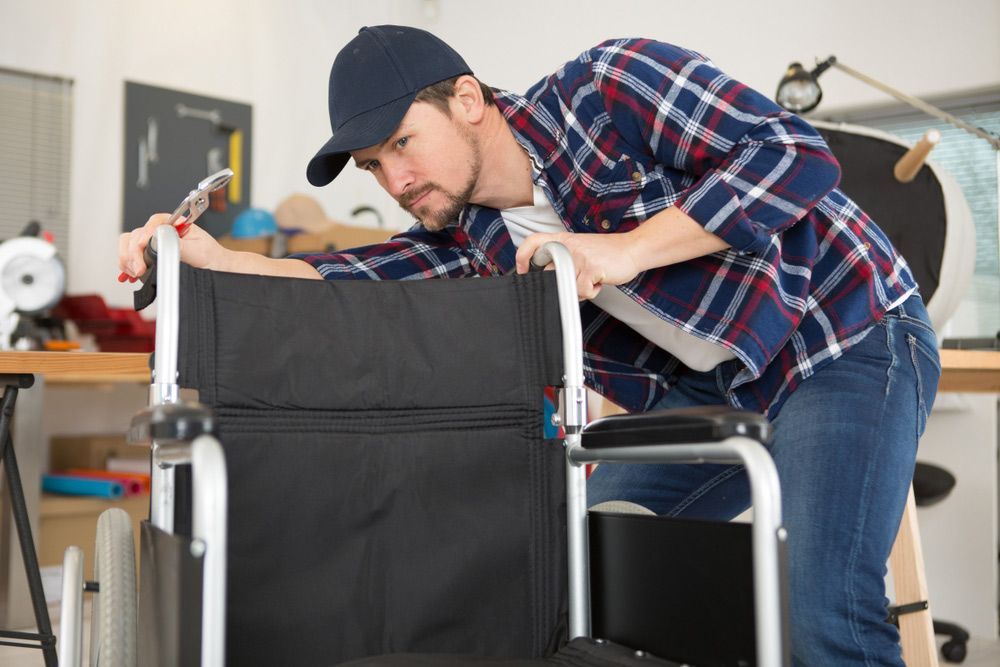 Man in a cap and flannel shirt using pliers to repair a manual wheelchair 
