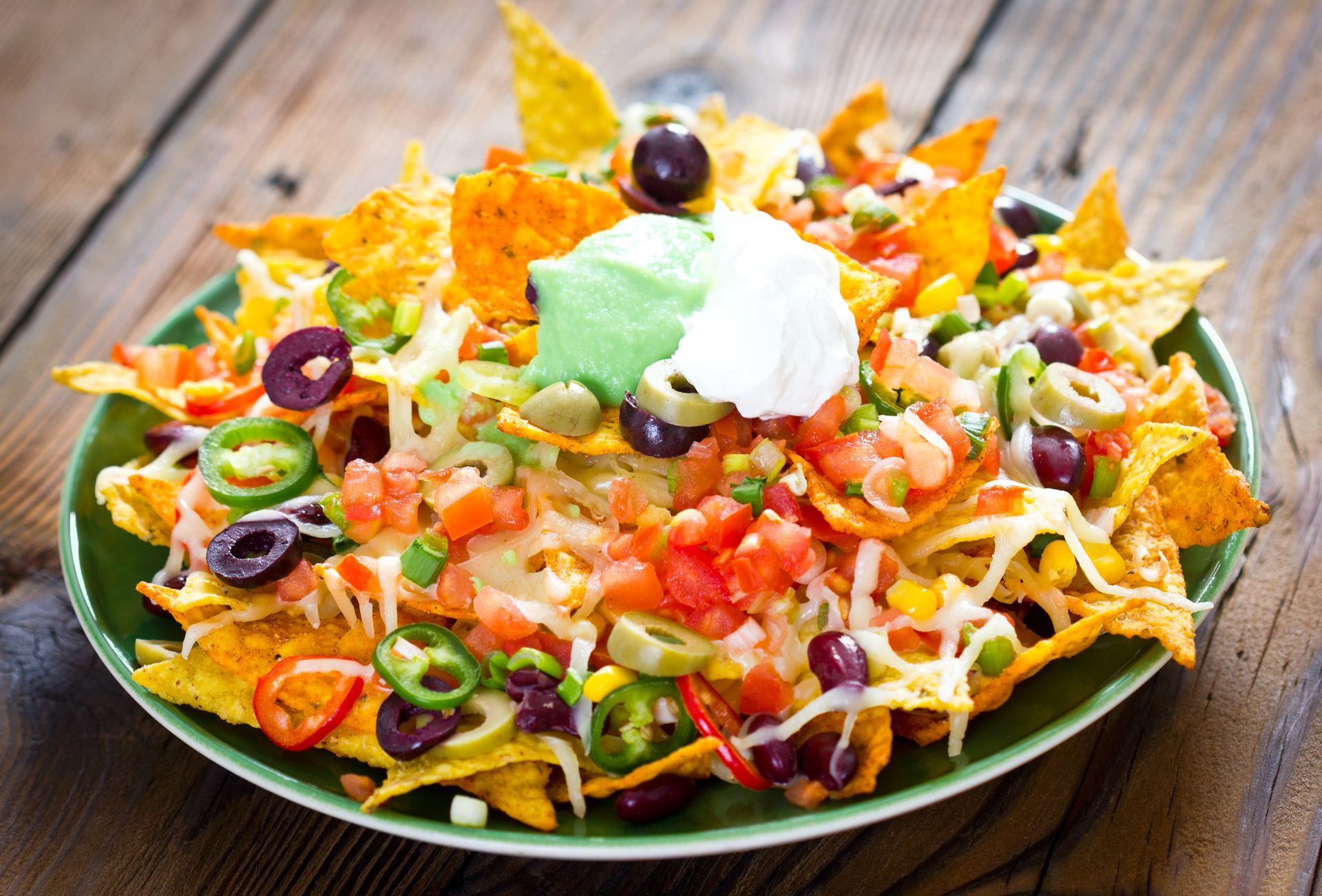 Nachos piled on a green plate, topped with salsa, olives, jalapeños, cheese, and sour cream.