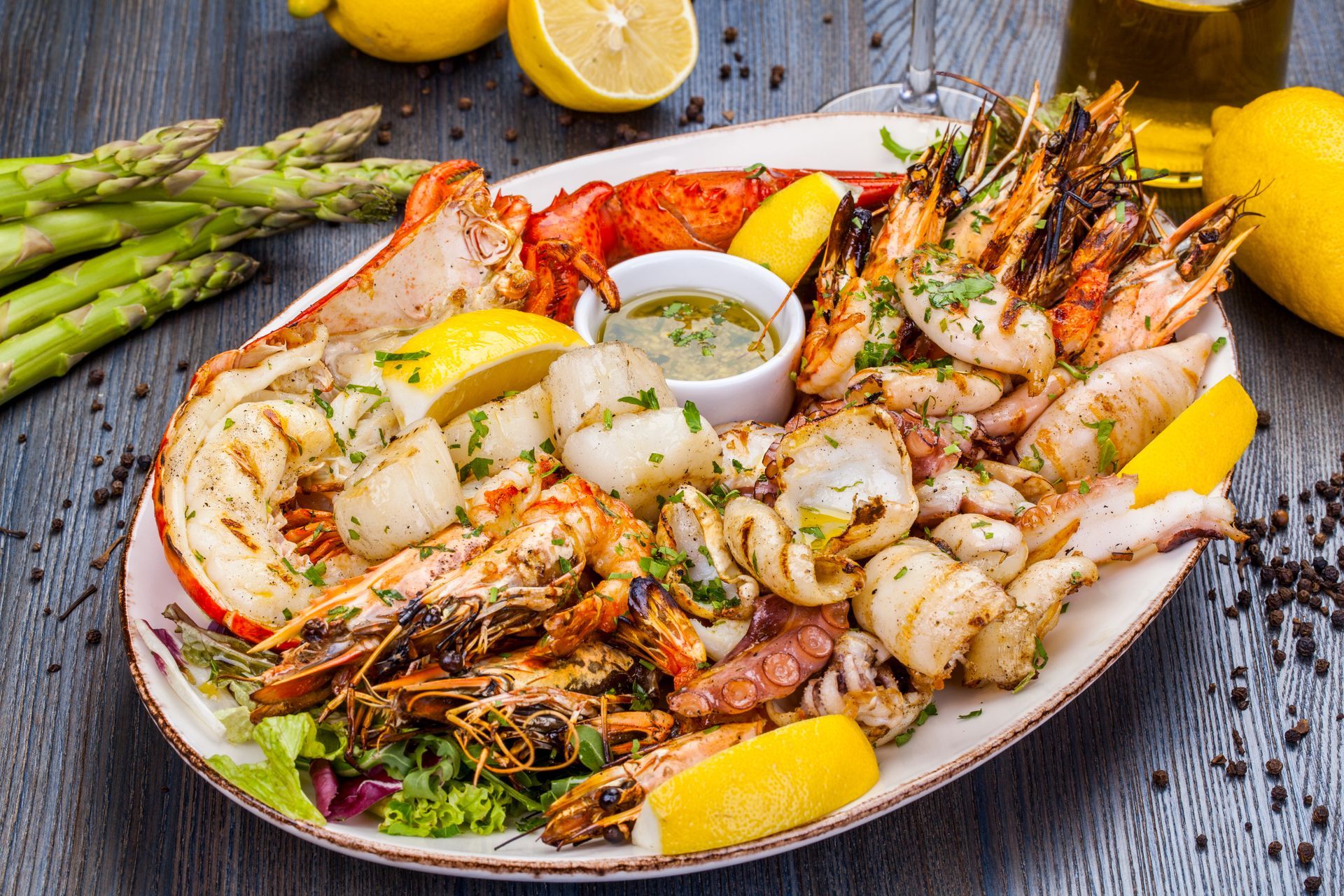 Grilled seafood platter with lobster, shrimp, scallops, and squid, served with lemon and asparagus.