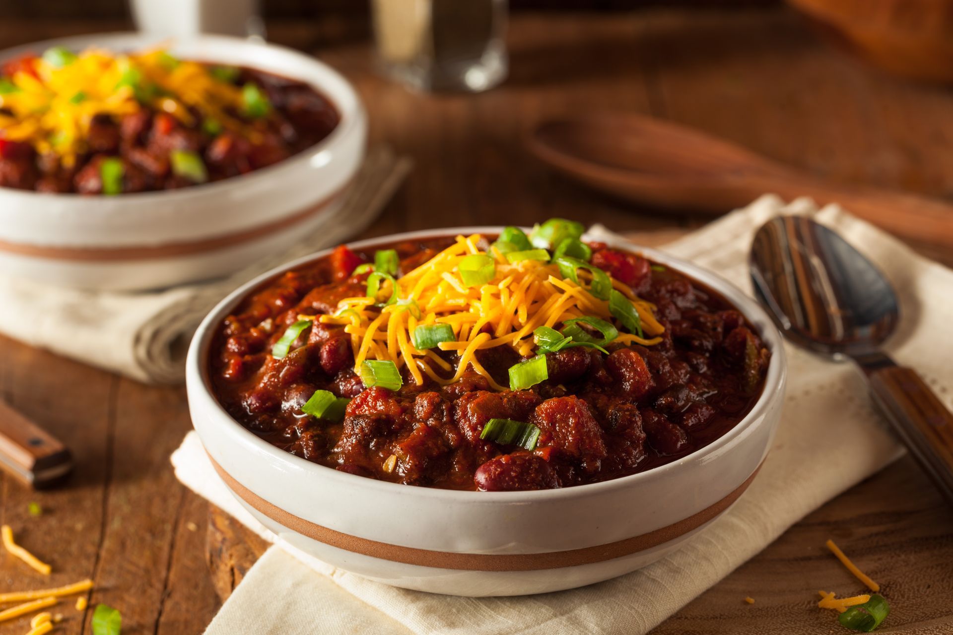 Bowls of chili topped with cheese and green onions, set on a wooden table.