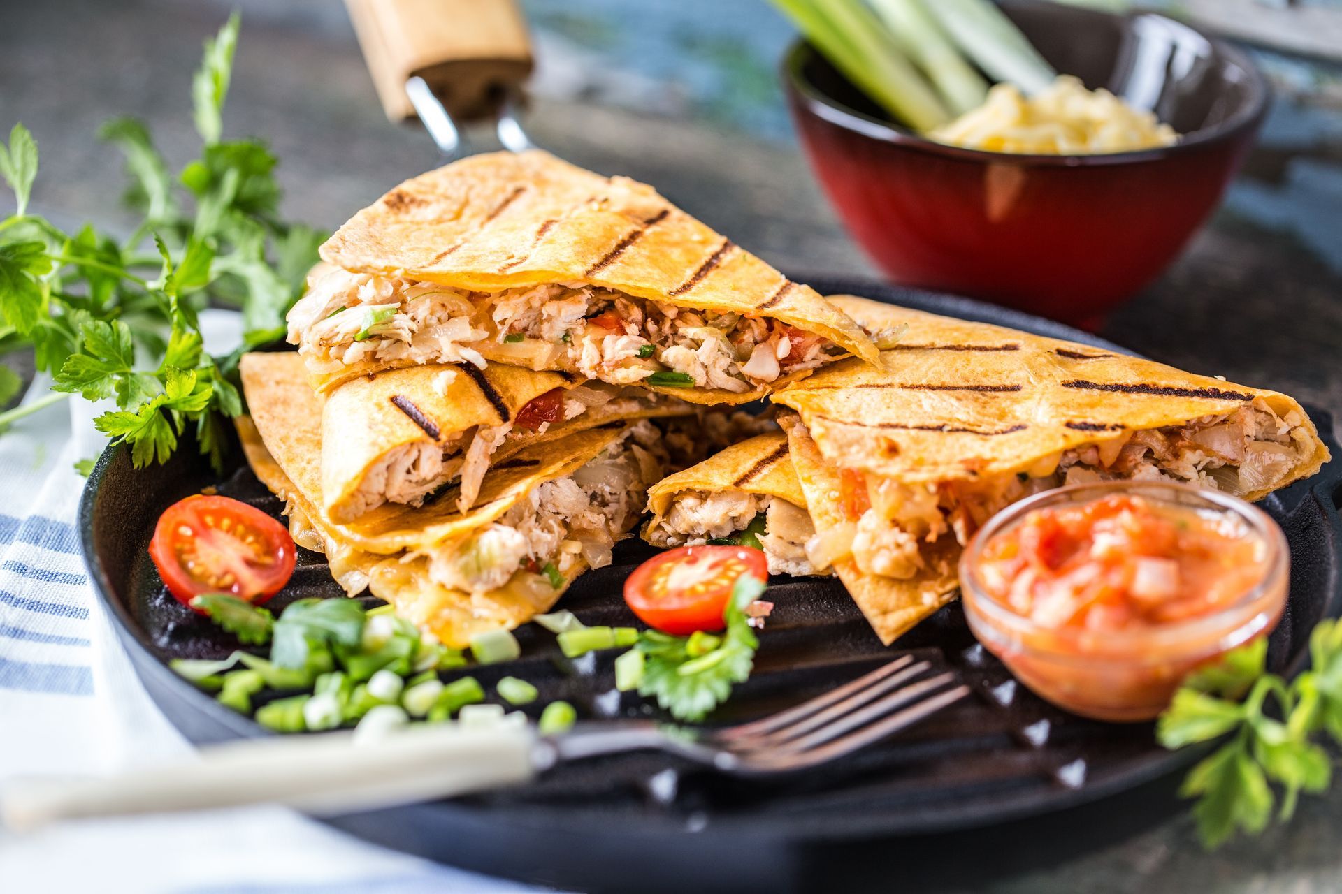 Grilled chicken quesadillas on a black grill pan with salsa, fresh herbs, and a bowl of dip.