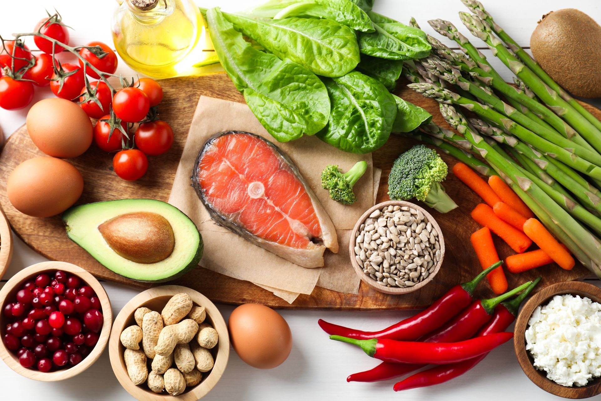 Assortment of fresh healthy foods, including salmon, eggs, vegetables, fruit, nuts, and seeds.
