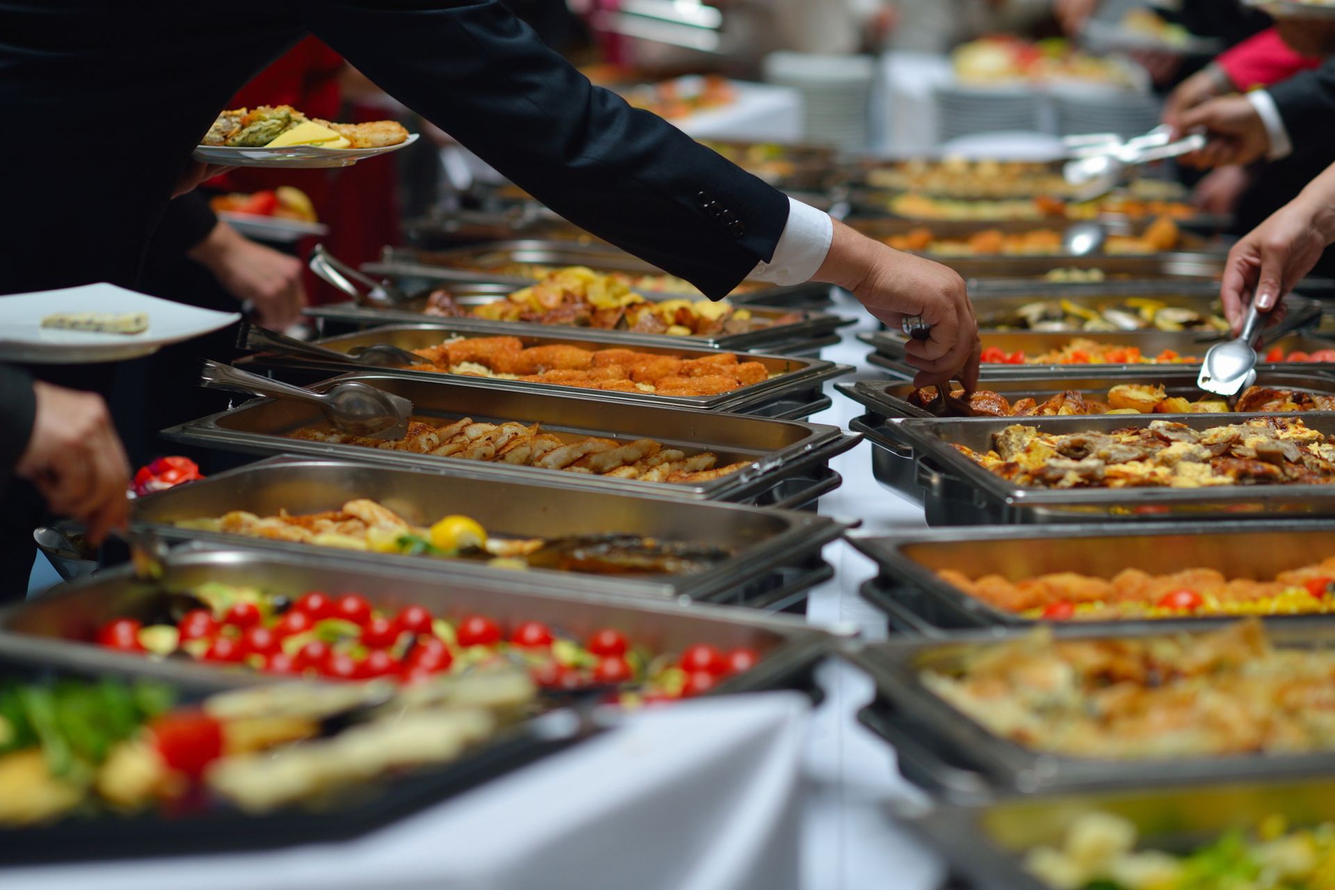 People serving food from buffet trays at a catered event.