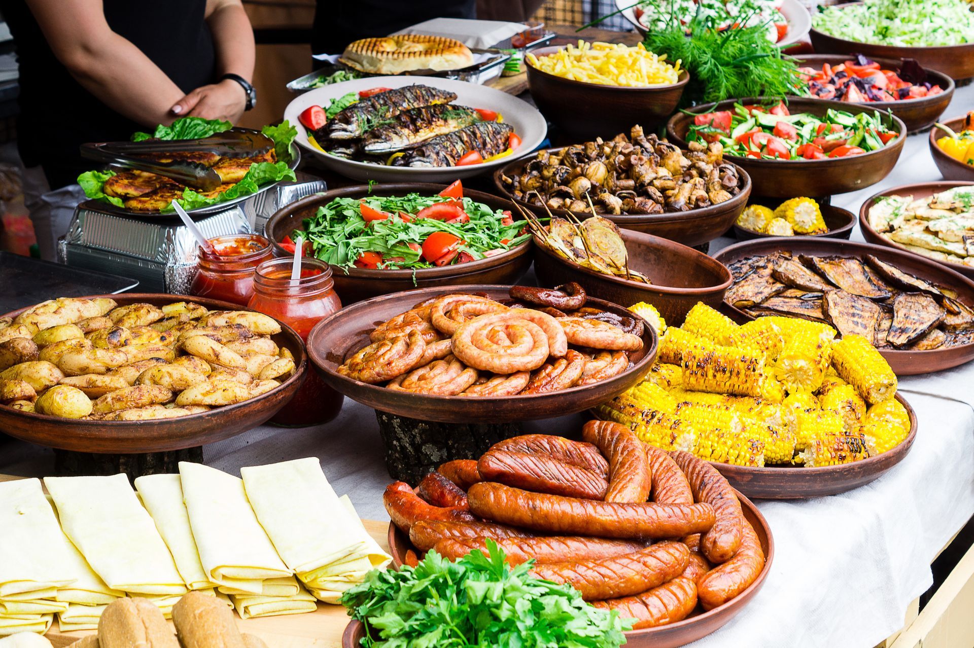 A table filled with a variety of cooked food, including sausages, corn, vegetables, and fish.