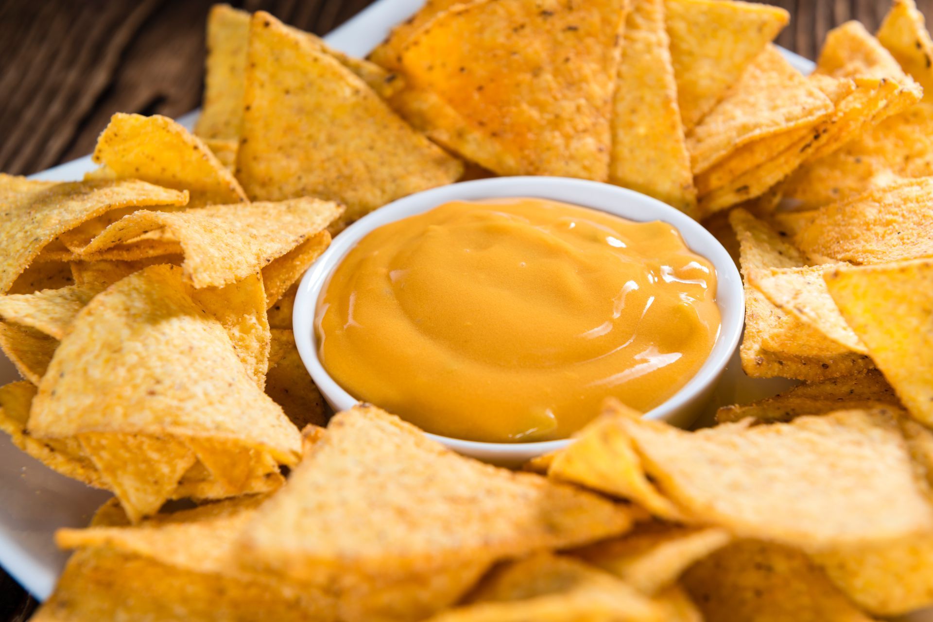 Tortilla chips surrounding a bowl of orange cheese dip.