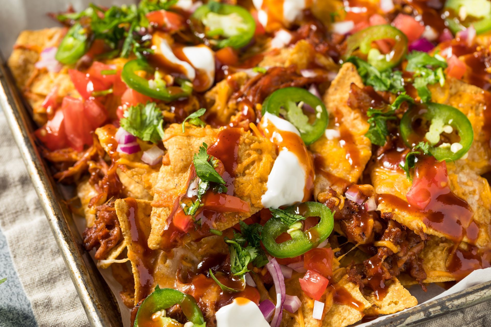 Loaded nachos with pulled pork, jalapeños, tomatoes, red onion, cilantro, sour cream, and BBQ sauce.
