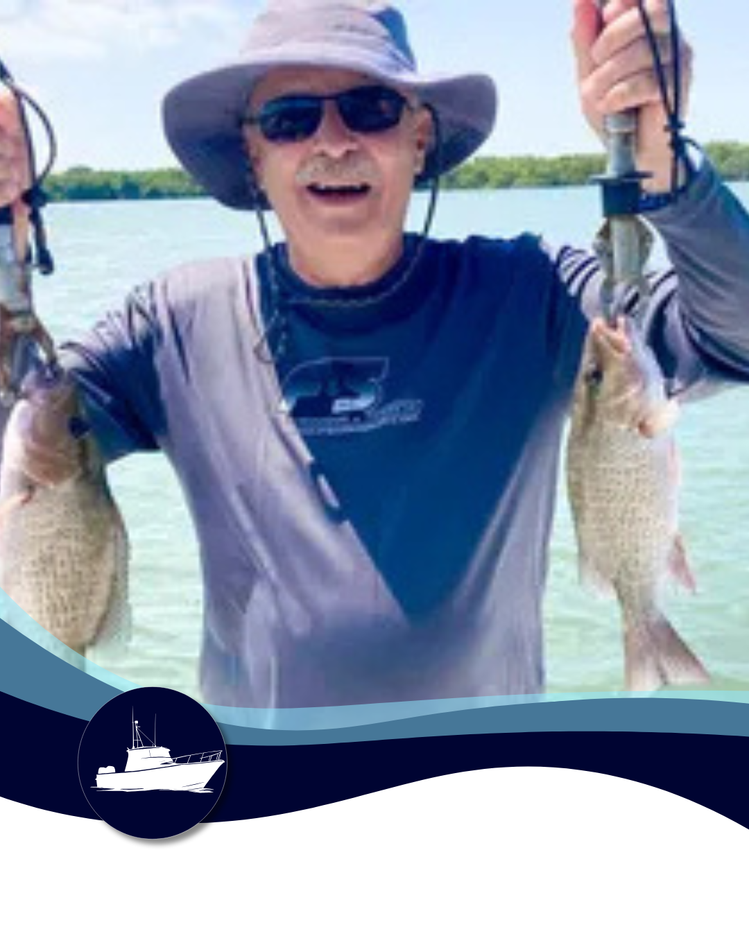 Man smiling while holding up two fish he caught, standing in the water. He wears sunglasses, a hat, and a blue shirt.