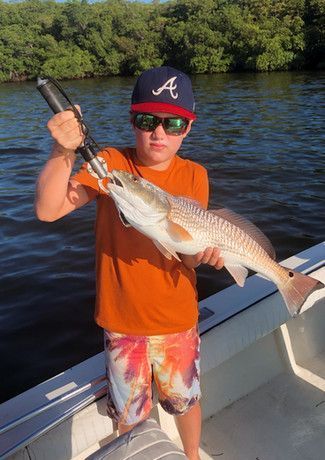Boy in orange shirt and sunglasses holds a large redfish on a boat, wearing an Atlanta Braves hat.