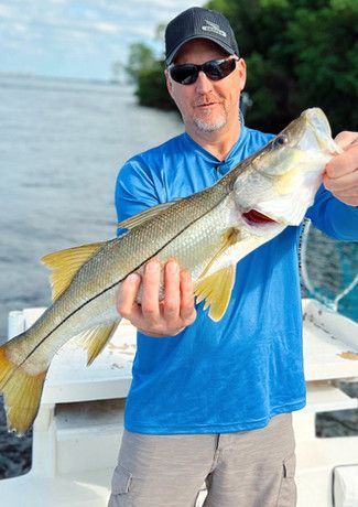 Man in sunglasses and blue shirt holding up a large fish with yellow fins on a boat.
