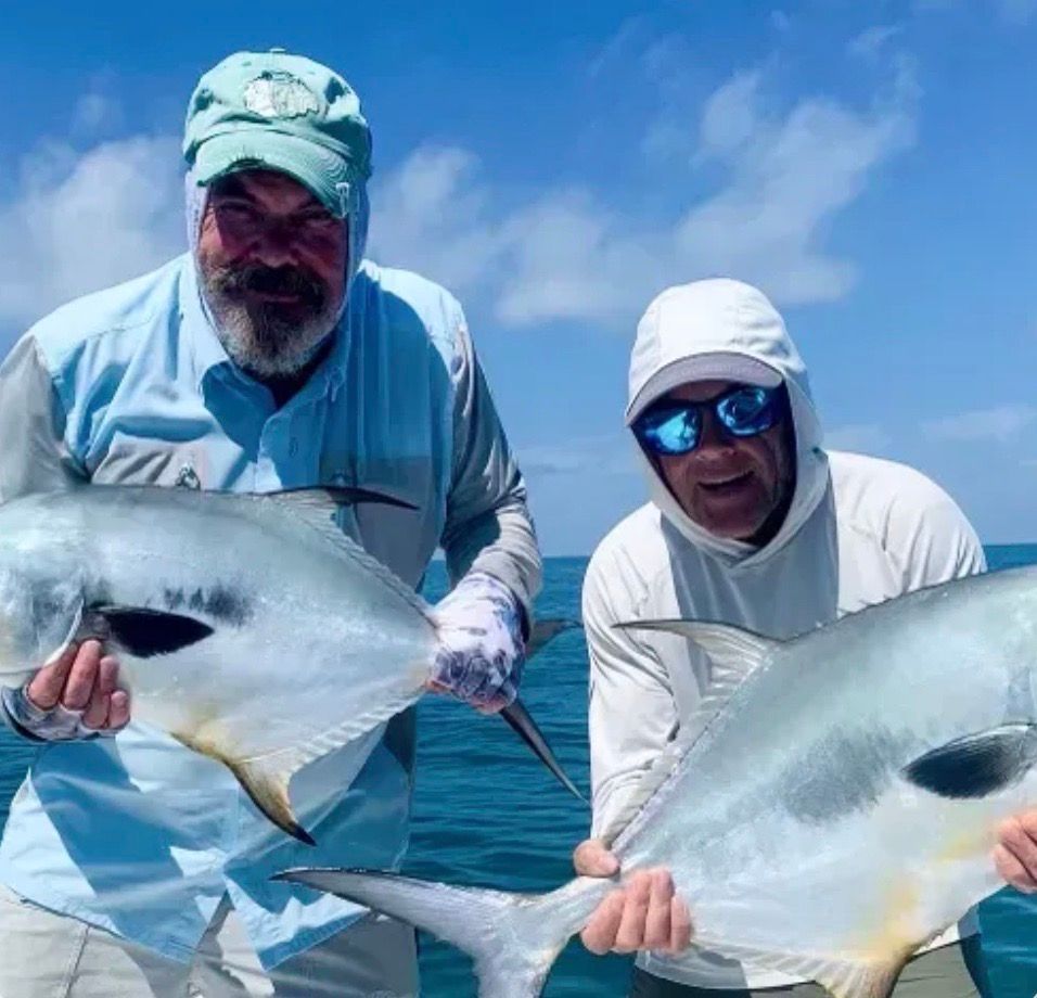 Two men on a boat holding large silver fish they caught, on a sunny day.