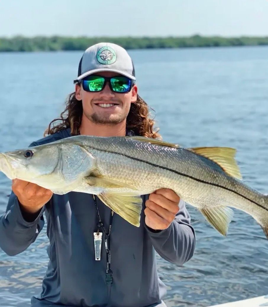 Man smiling, holding a silver and yellow fish on a boat, with water and sky in the background.