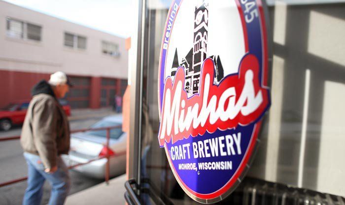 A Minhas Craft Brewery sign on a glass door, with a person walking on the street in the background.