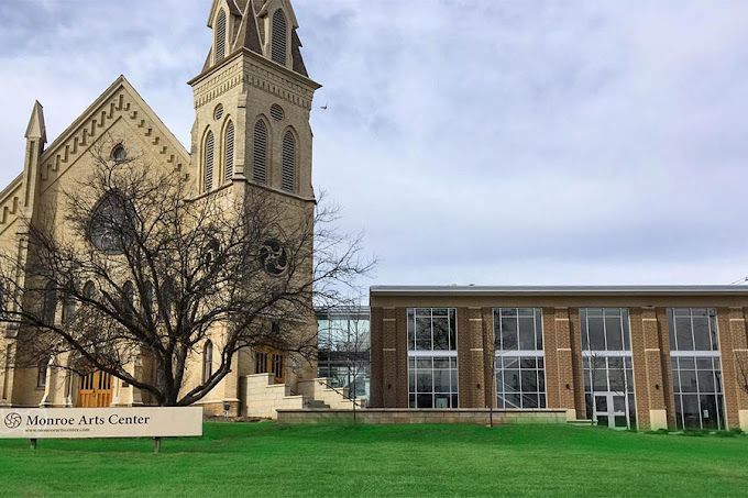 A stone church with a tall steeple stands beside a modern brick building labeled 