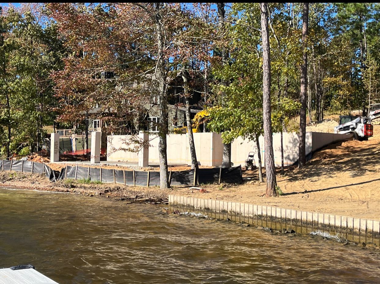 A sea wall is being built on the shore of a lake surrounded by trees.