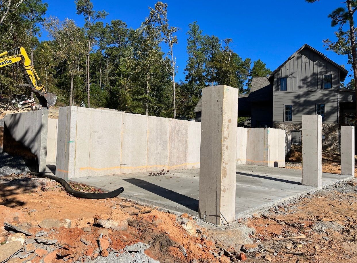 A construction site with a house in the background and a yellow excavator in the foreground.
