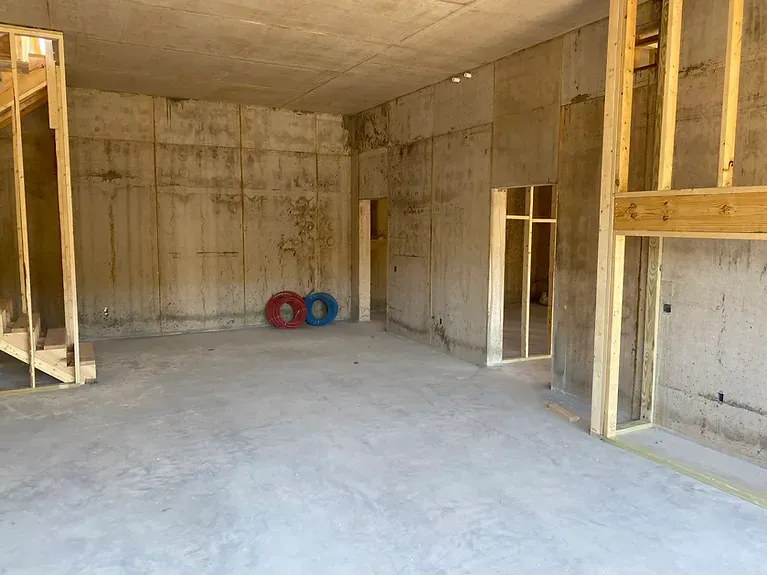 A large empty room with concrete walls and a wooden staircase.