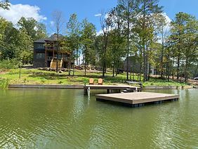 There is a dock in the middle of a lake with a house in the background.