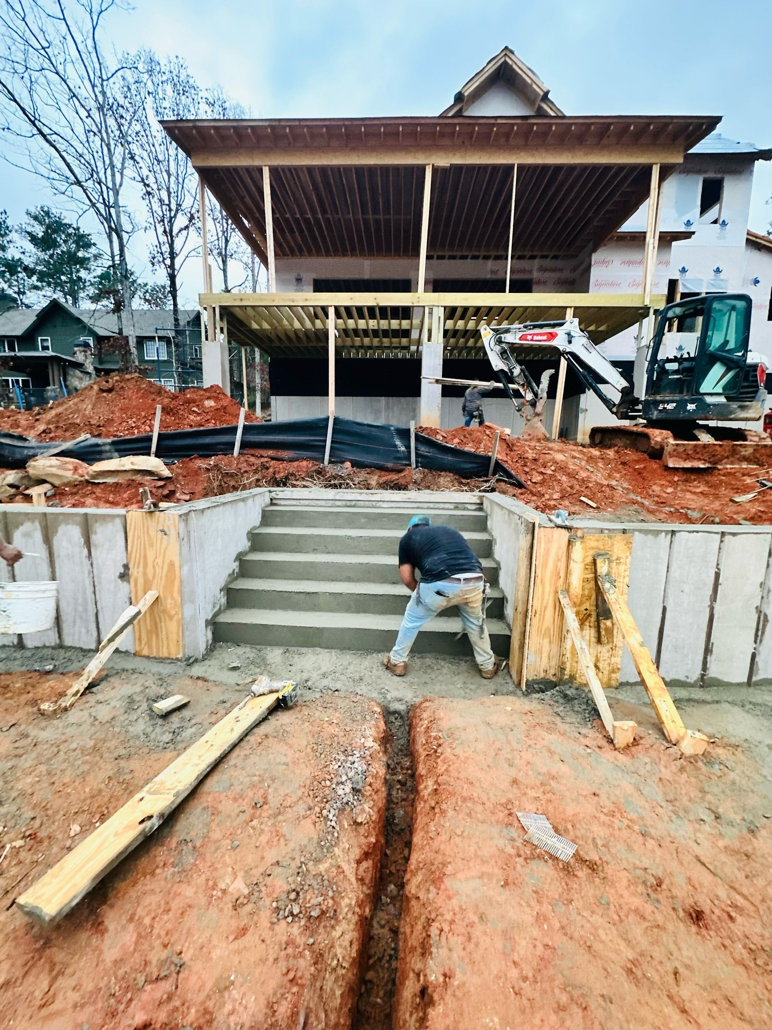 A man is digging a trench in front of a house under construction.