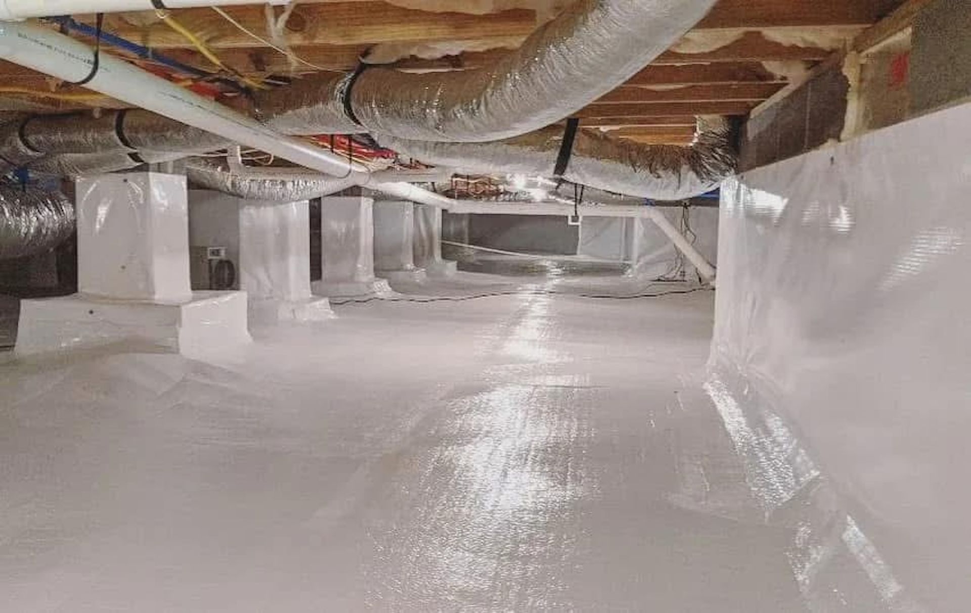 A crawl space encapsulated with white vapor barrier plastic on the floor, walls, and support pillars.
