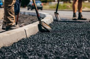 Workers paving a curbside road with hot asphalt and shovels