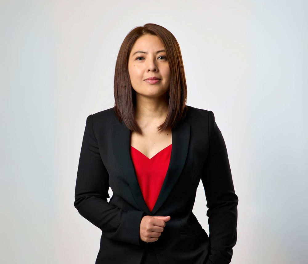 A woman in a black suit and red top is standing with her hands in her pockets.
