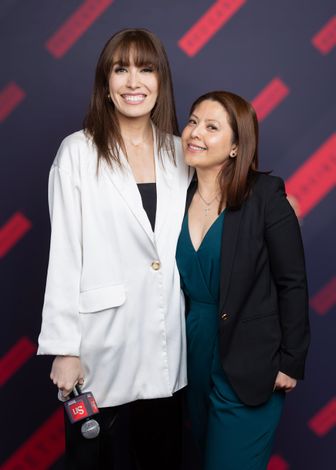 Two women are posing for a picture together and one is holding a microphone.