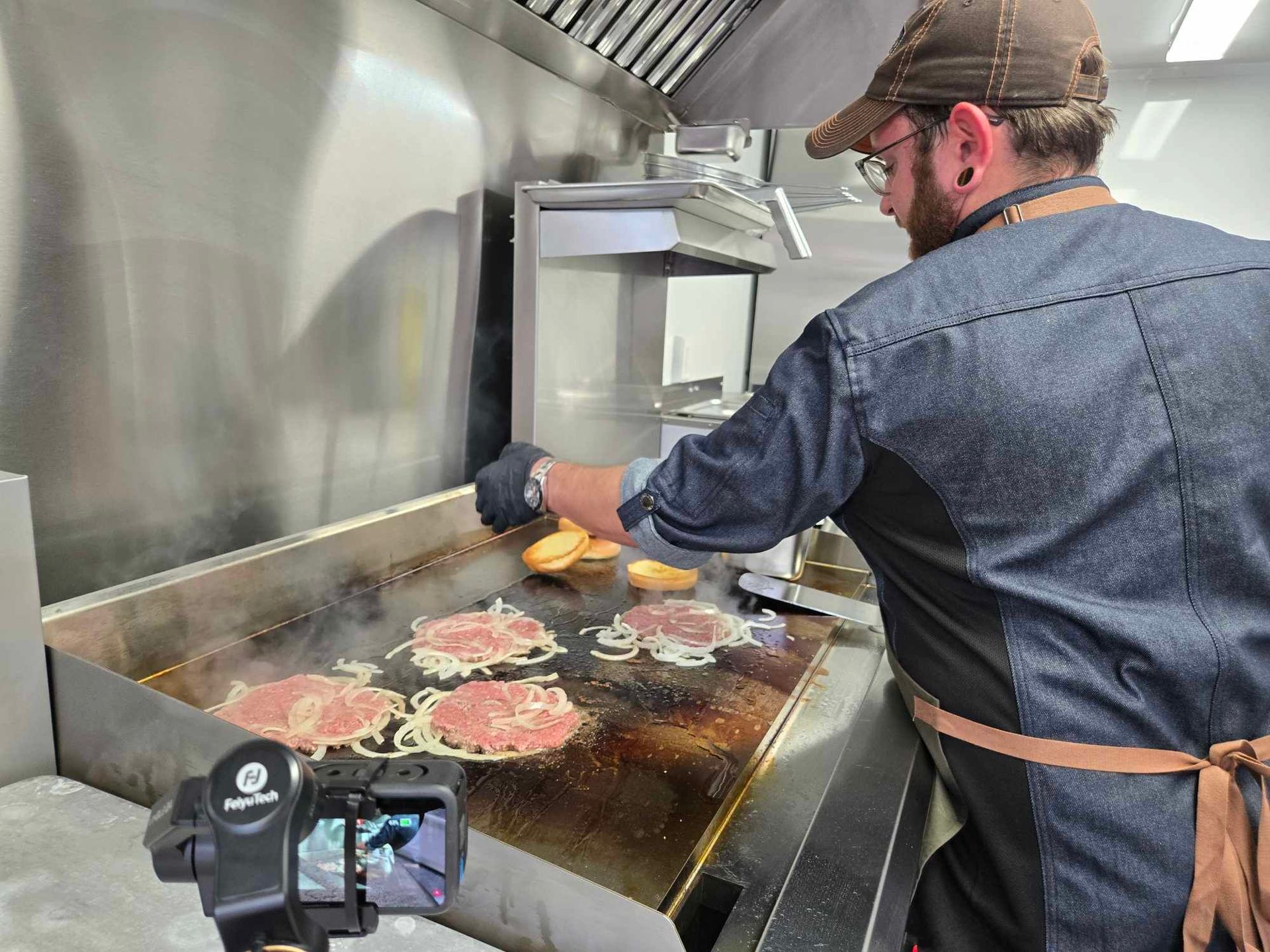 Owner preparing smash burgers with onions in a food truck.