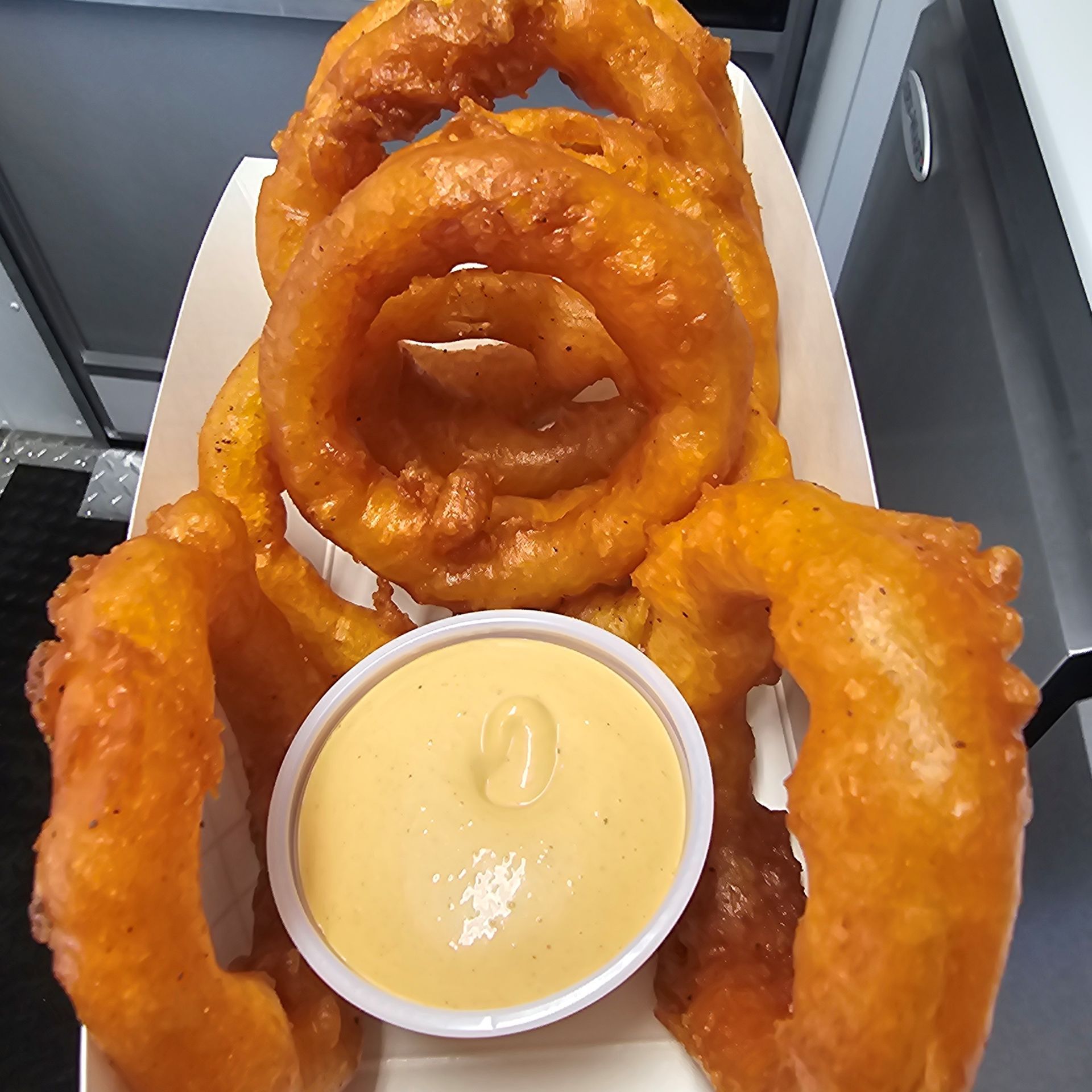 A tray of onion rings with a small bowl of sauce.