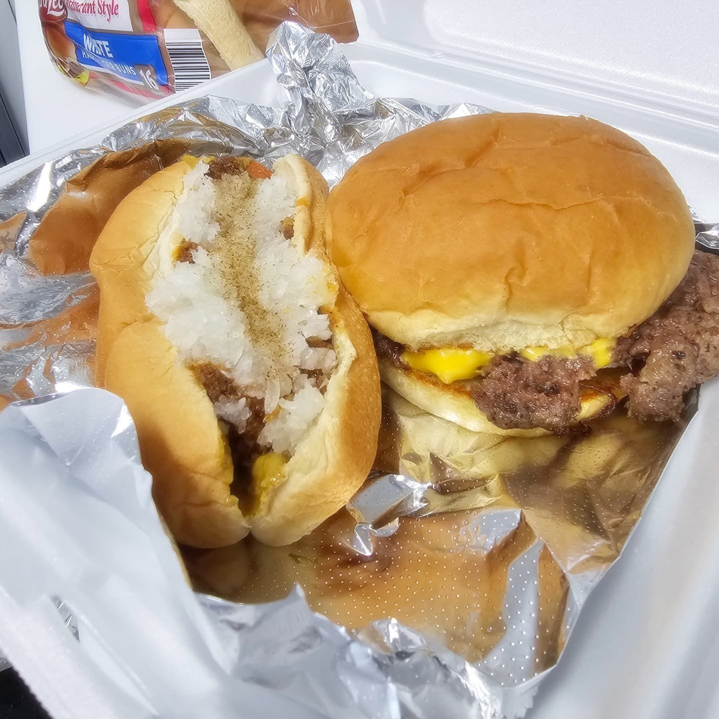 Two hamburgers are wrapped in tin foil in a styrofoam container.