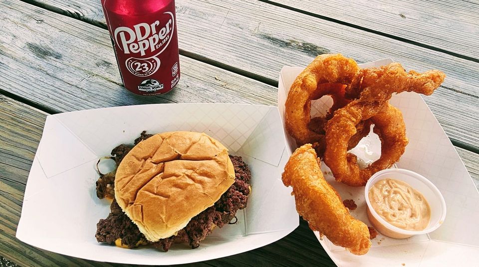 Smash burger, onions rings, and a drink on a bench.