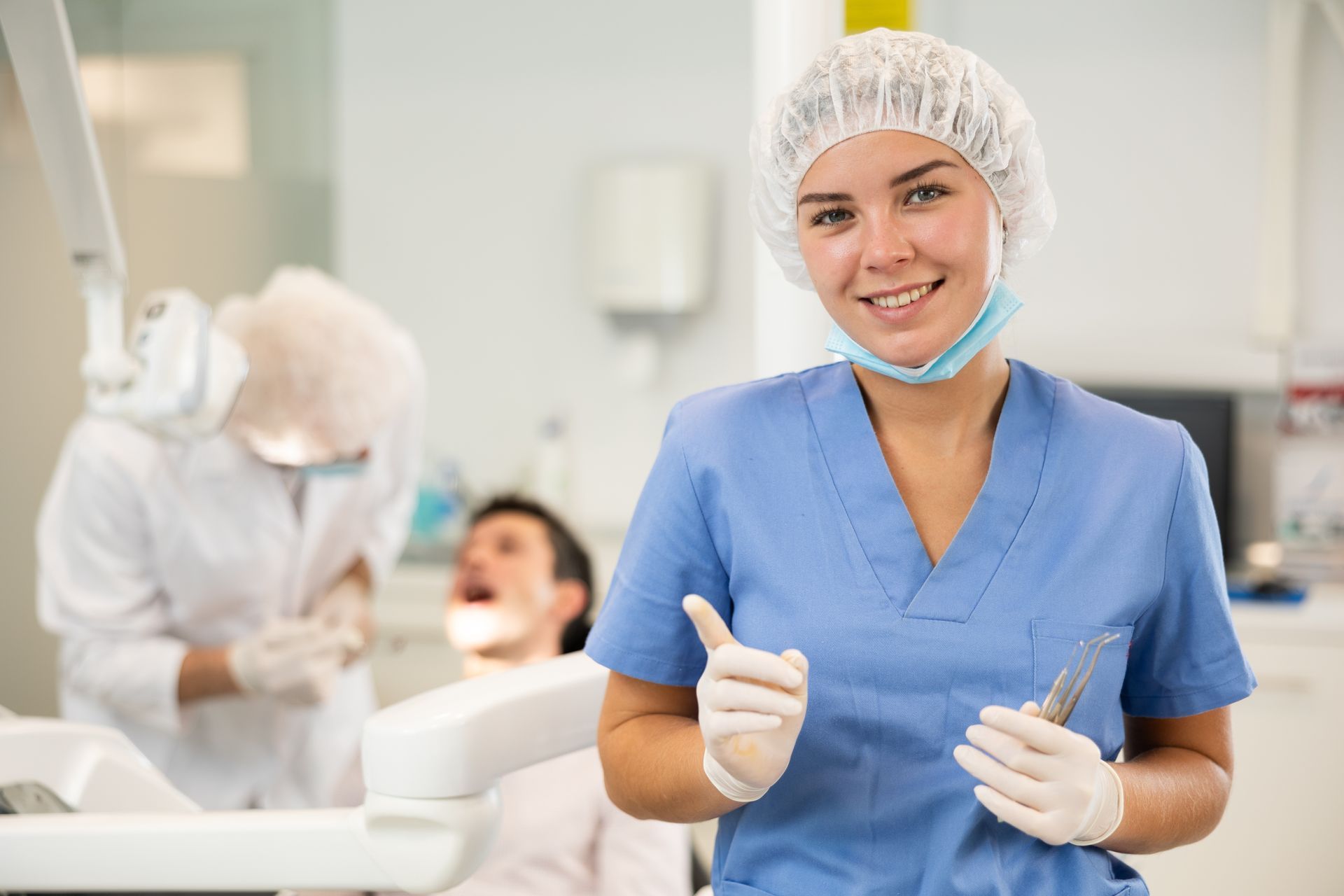 General dentist smiling in blue scrubs holding dental tools in modern clinic setting.