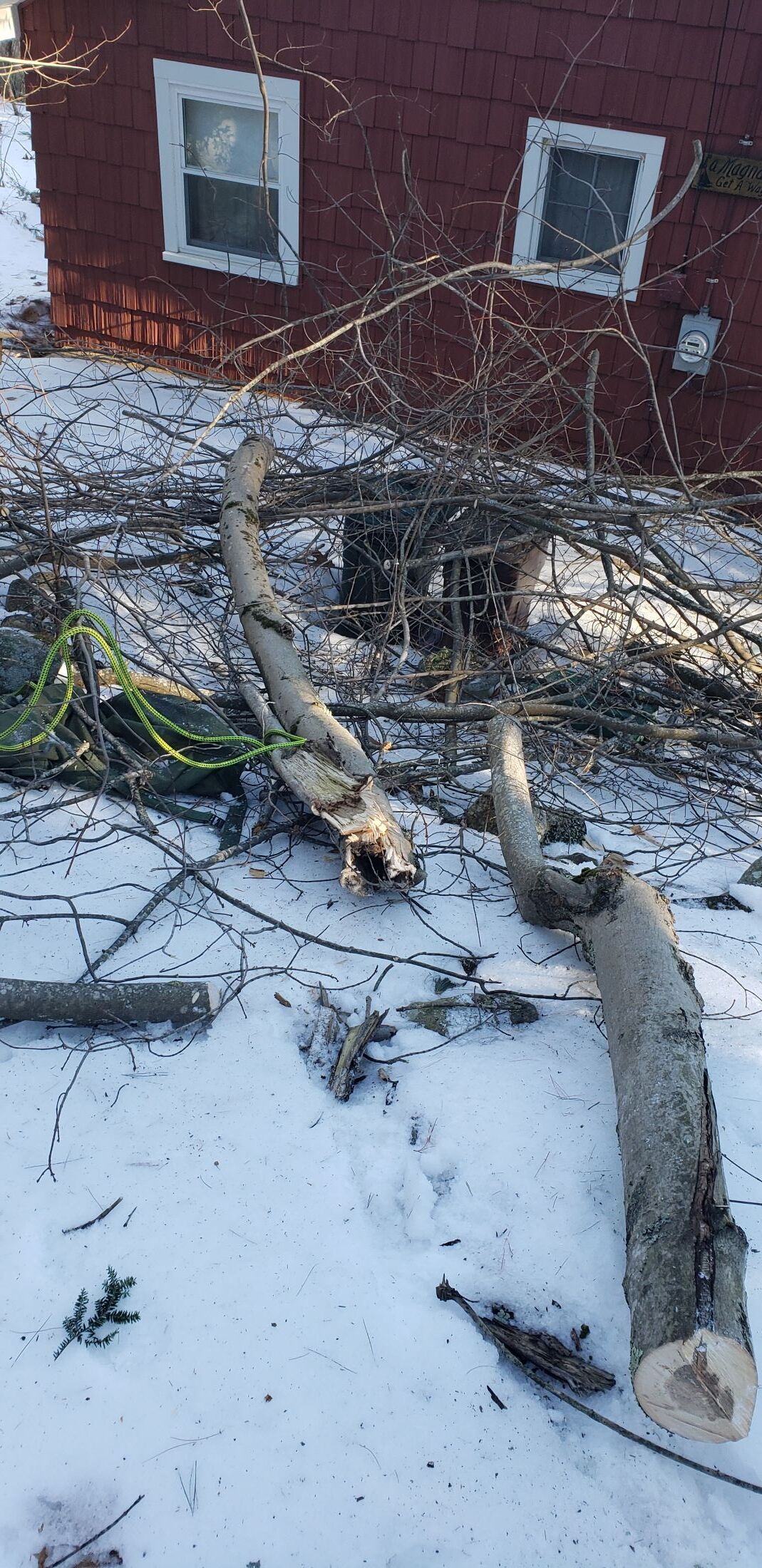 A pile of logs in the snow in front of a red house.