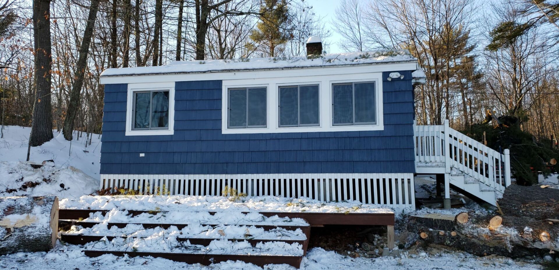A blue house with a white deck and stairs in the snow