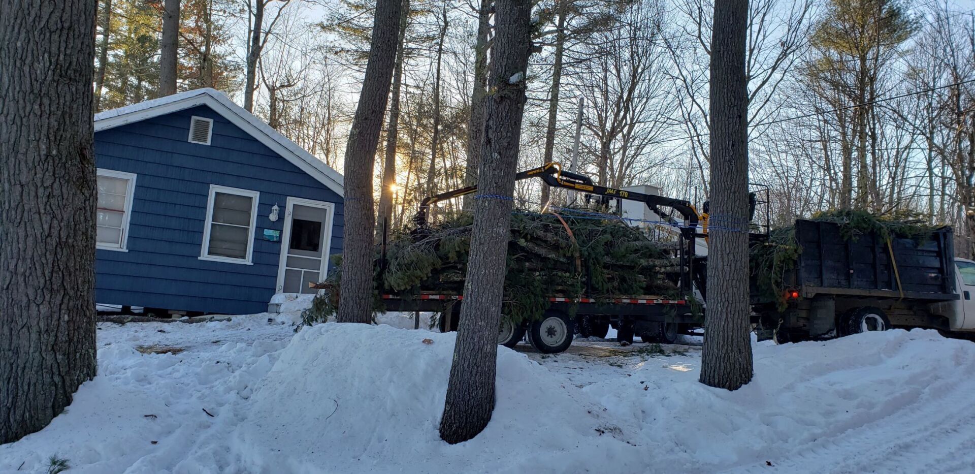 A truck is carrying a christmas tree to a house in the snow.
